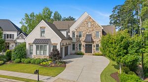 Aerial drone view of luxurious stone mansion with curved driveway and manicured landscaping in an upscale neighborhood. Real estate photo.