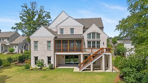A panoramic view of modern farmhouse-style homes with white exteriors nestled among green trees and landscaping. Real estate photography.