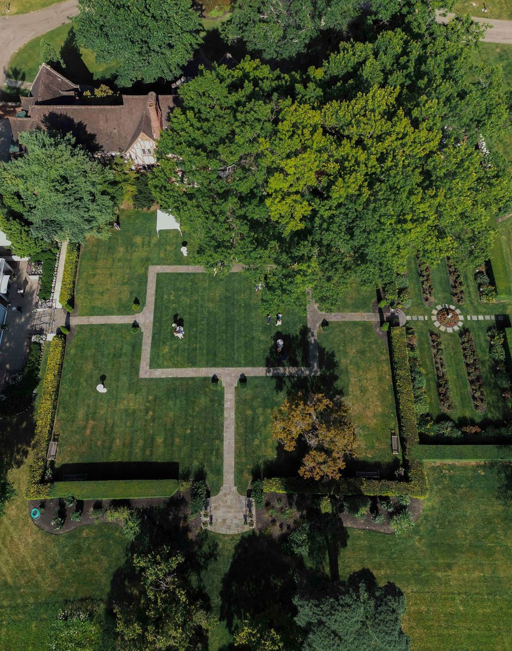 Aerial view of a formal garden with manicured lawns, geometric pathways and lush green trees surrounding the space.