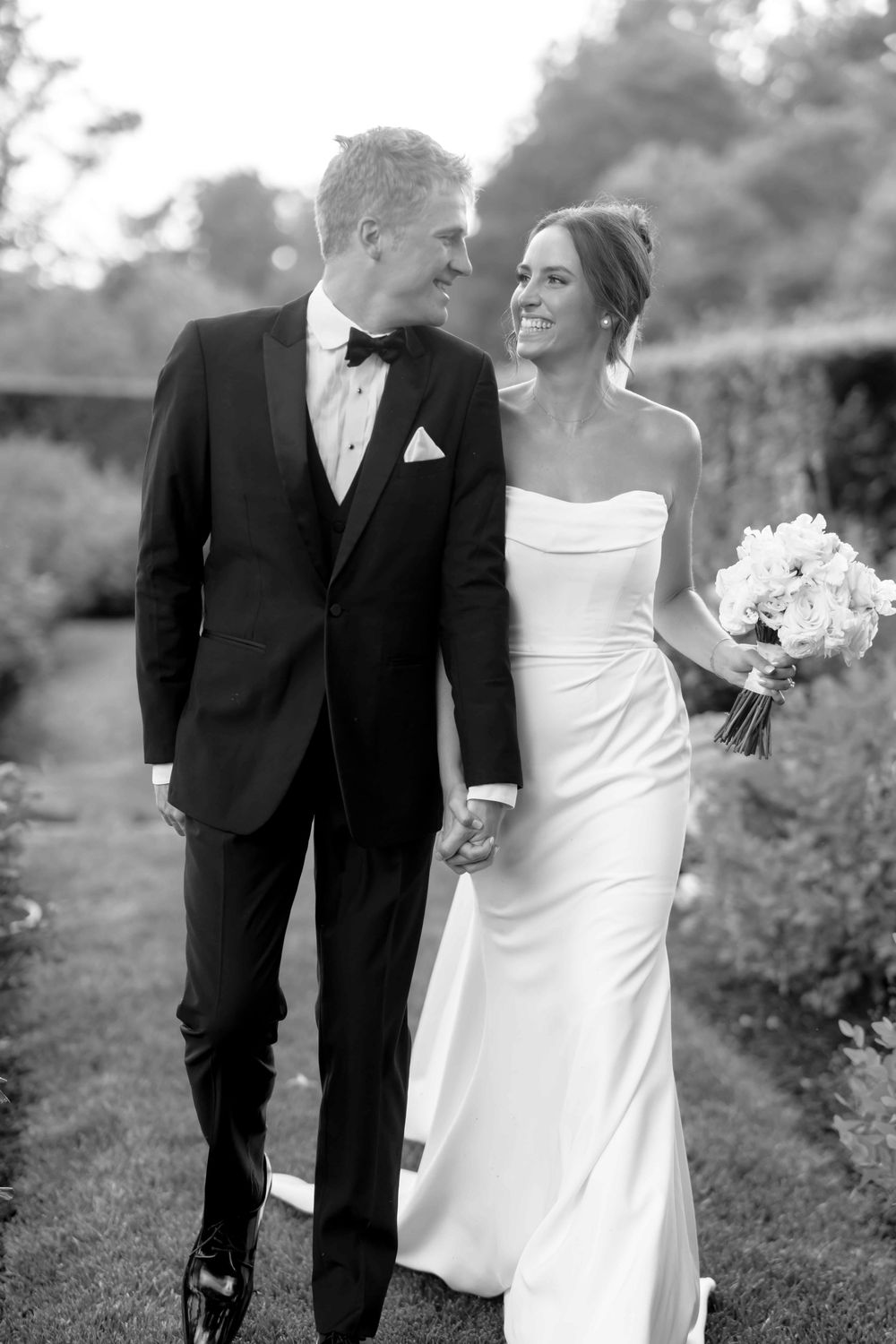 A series of romantic black and white wedding photos showing a couple in formal attire walking outdoors.