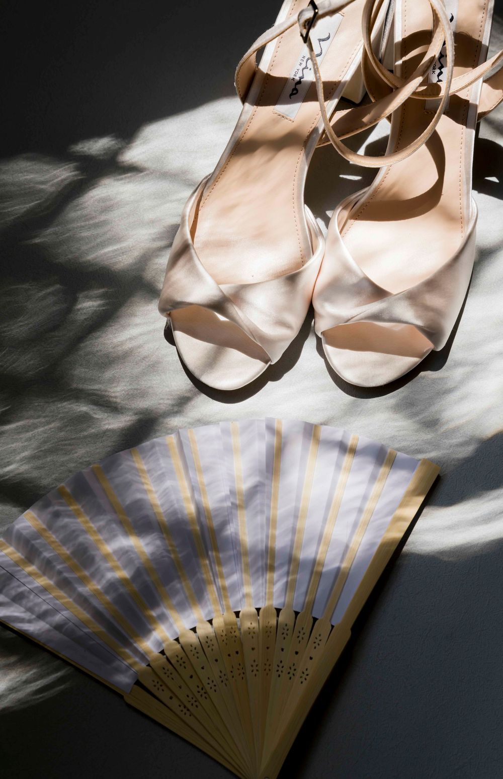 Pink ballet slippers and a blue striped decorative fan arranged on a dark contrasting surface with dramatic lighting.