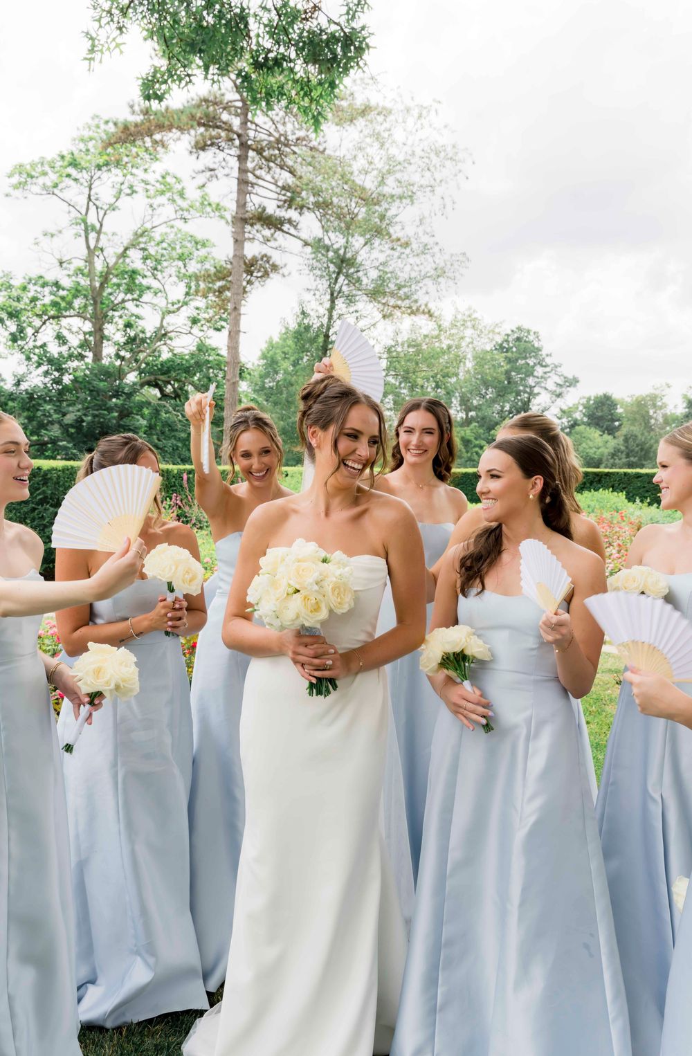 Bridal party in light blue bridesmaid dresses gathered outdoors with bouquets.
