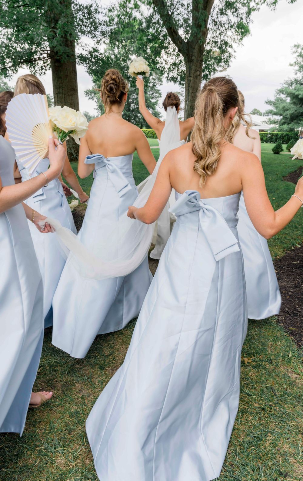 Bridesmaids in light blue strapless dresses with bows walking together outdoors.
