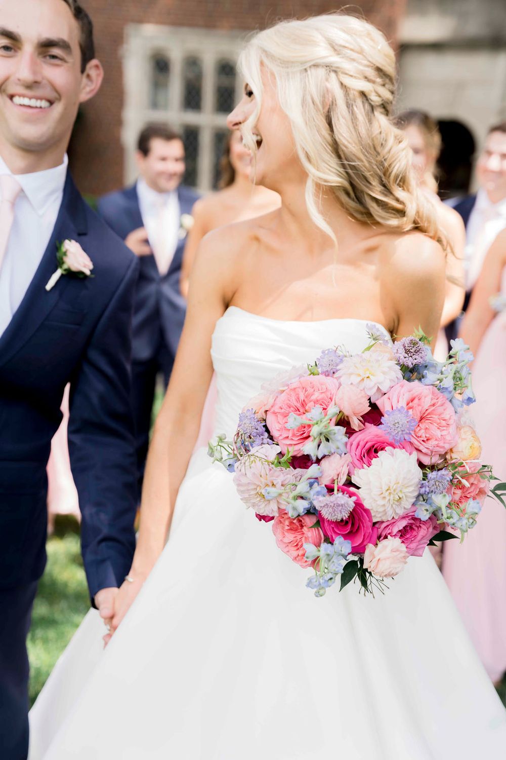 A joyful wedding moment captured with a beautiful bouquet of pink and purple flowers against a white gown.