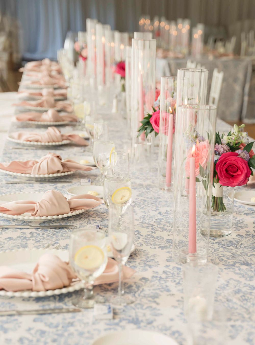 Long wedding reception table with pink accents, crystal glasses, and floral centerpieces.