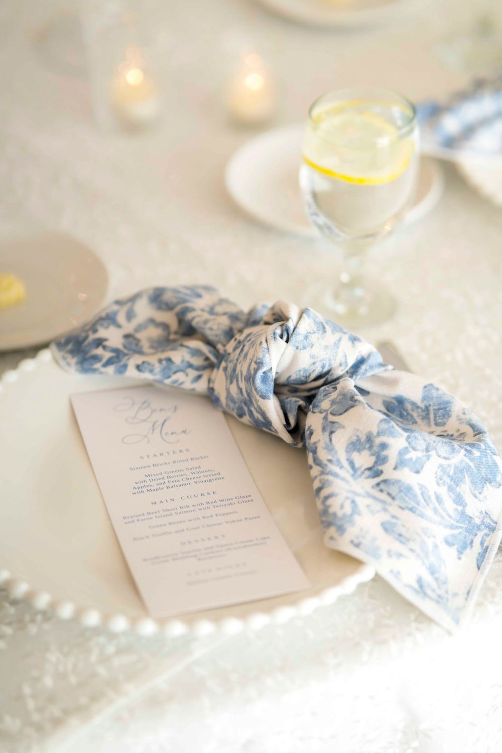 Wedding menu card with blue floral napkin and lemon water on white plate.