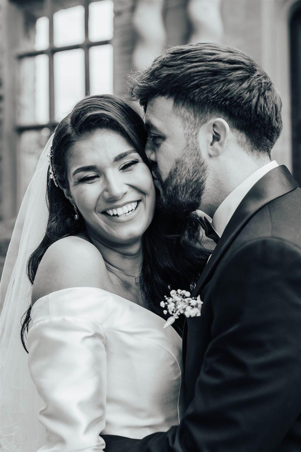 A joyful black and white wedding photo showing candid moment between bride and groom with bride laughing at camera.