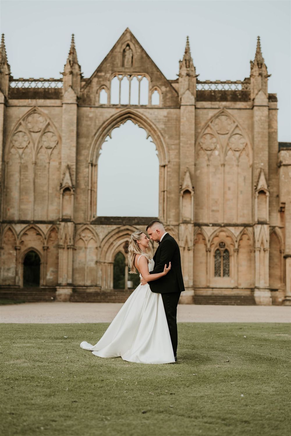 A couple shares an intimate moment on the lawn in front of Newstead abbey ruins with ornate stone archways.