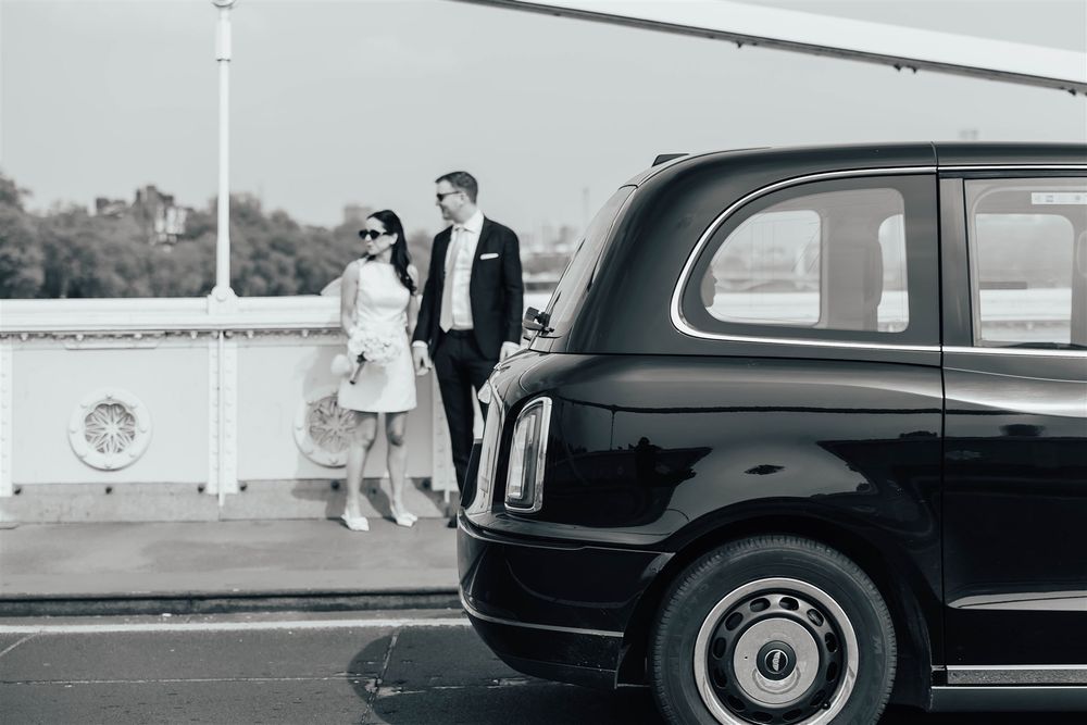 Classic black and white editorial style image of stylish wedding couple on Albert bridge, London with black cab driving through the image.