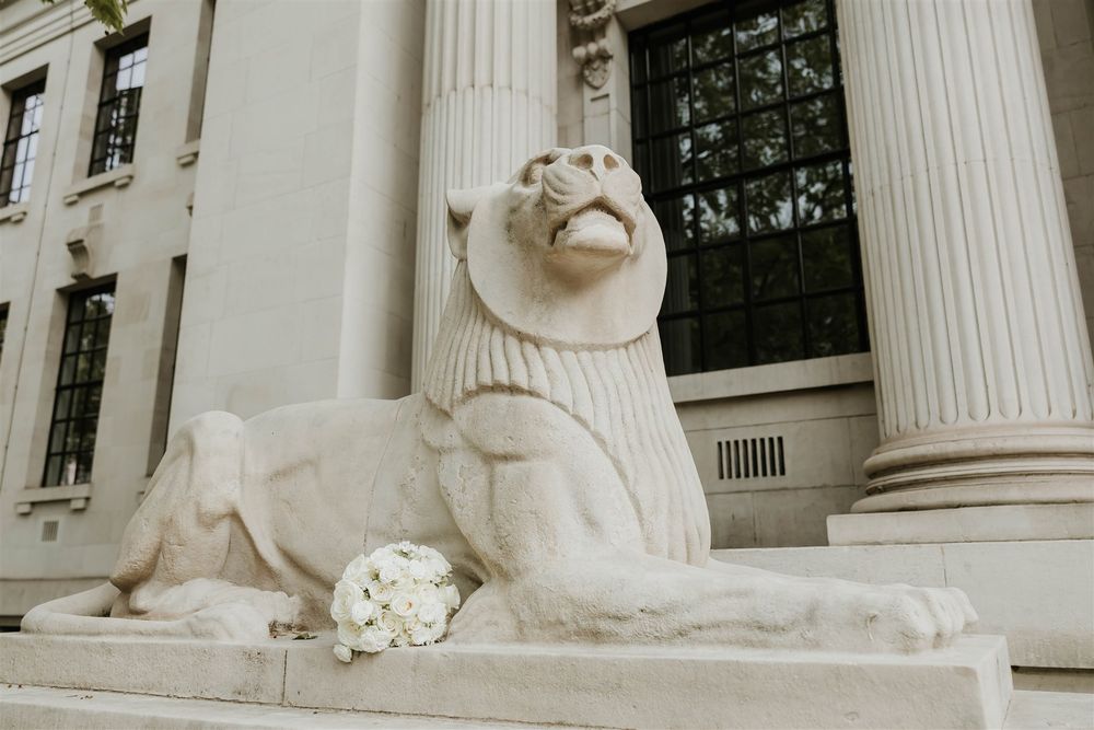 A majestic stone lion statue rests beside white classical columns at the entrance of Old Marylebone town hall, London