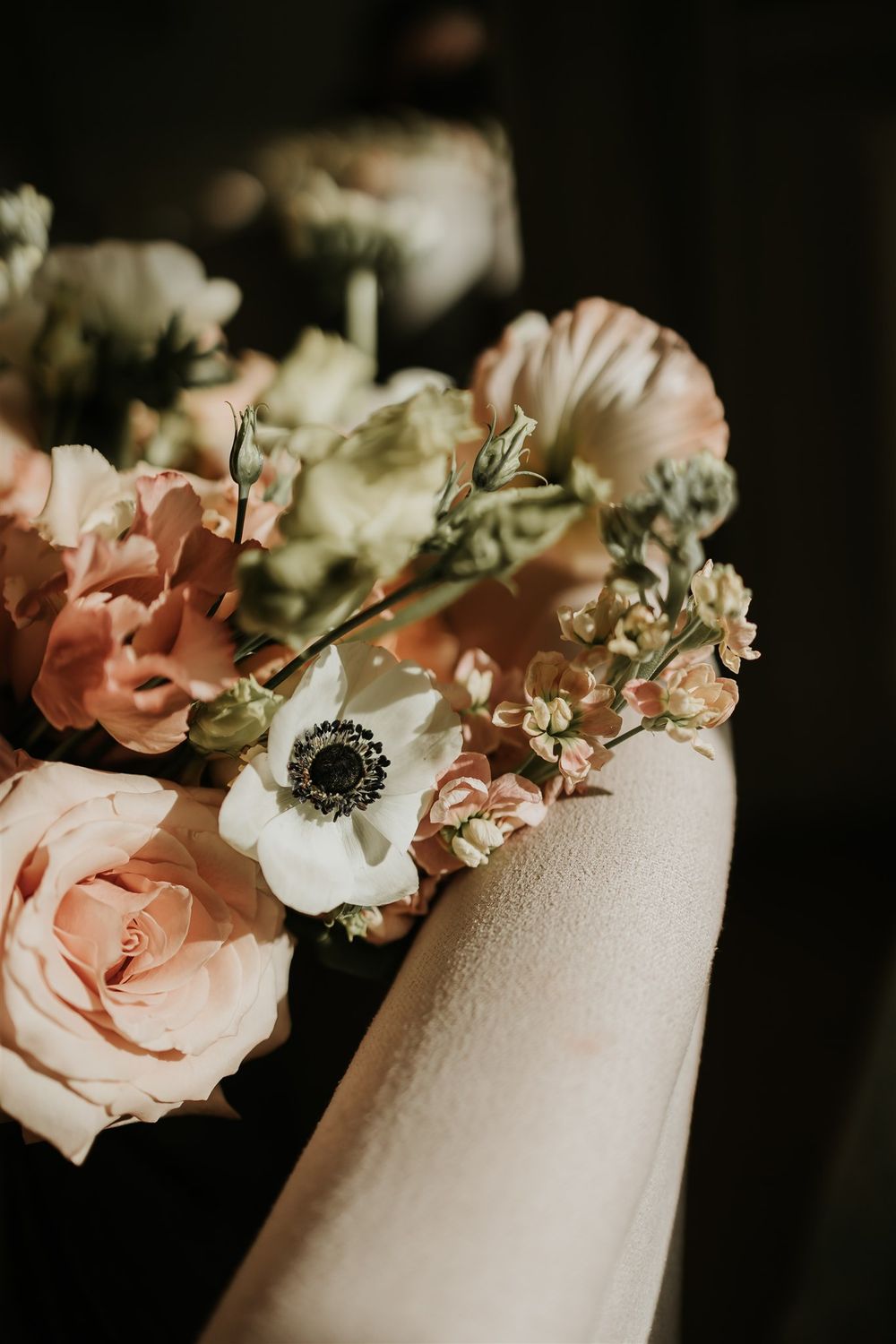 A moody floral arrangement featuring pink roses and white anemones against a dark background.