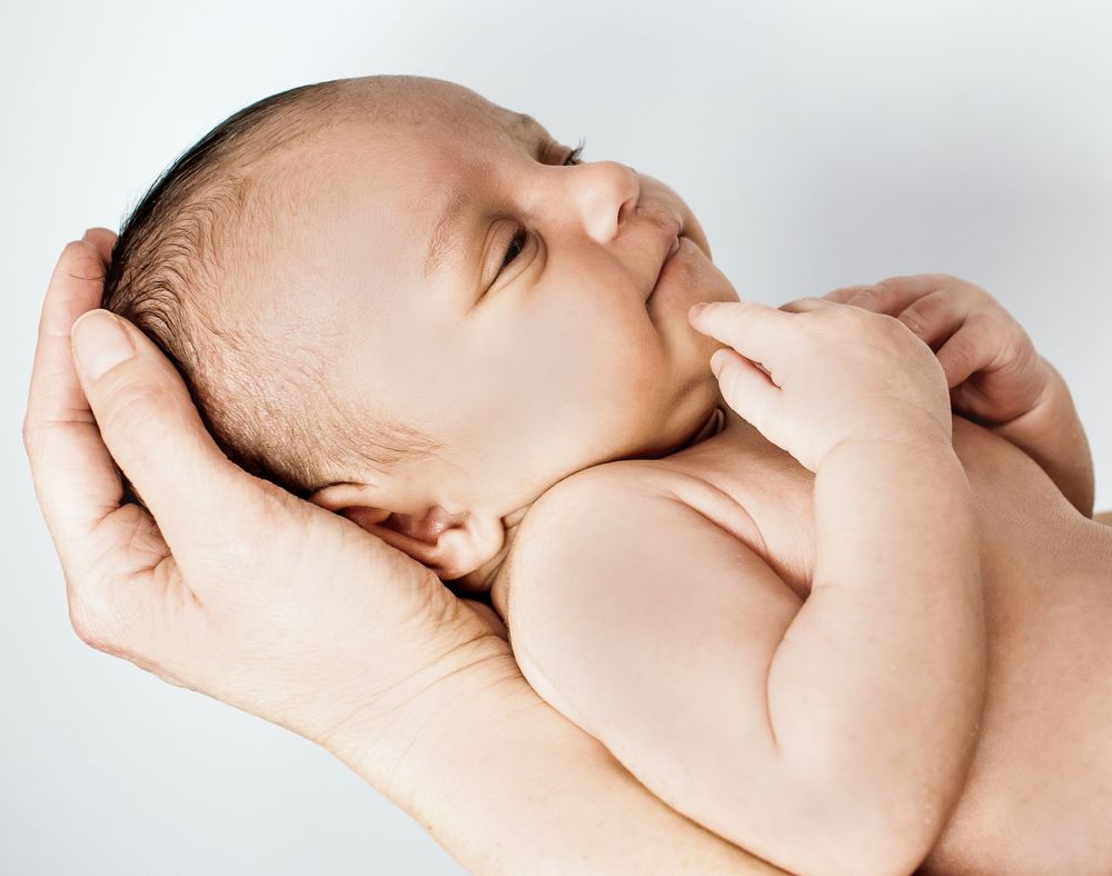 Adult hands gently hold a peaceful sleeping newborn baby against a white background.