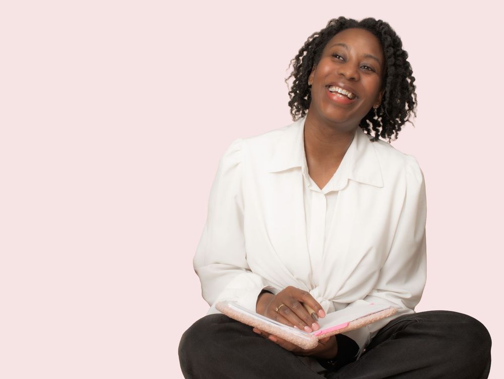 Professional headshot against pink background showing subject wearing a white button-up blouse and dark pants.