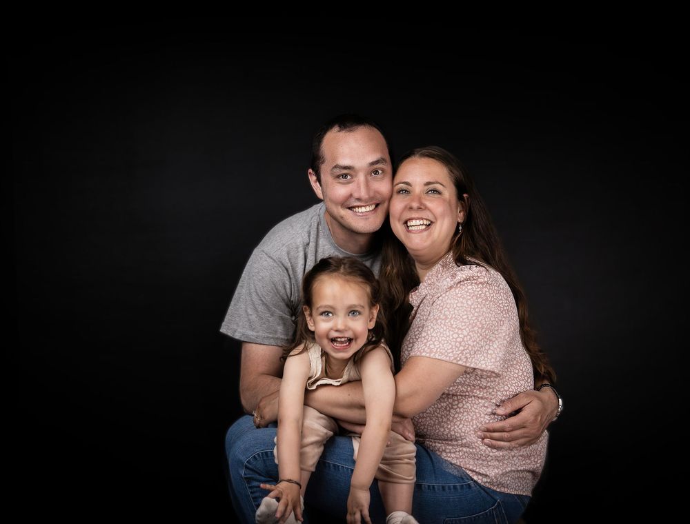 Portrait of a happy family of three smiling together against a black studio background.