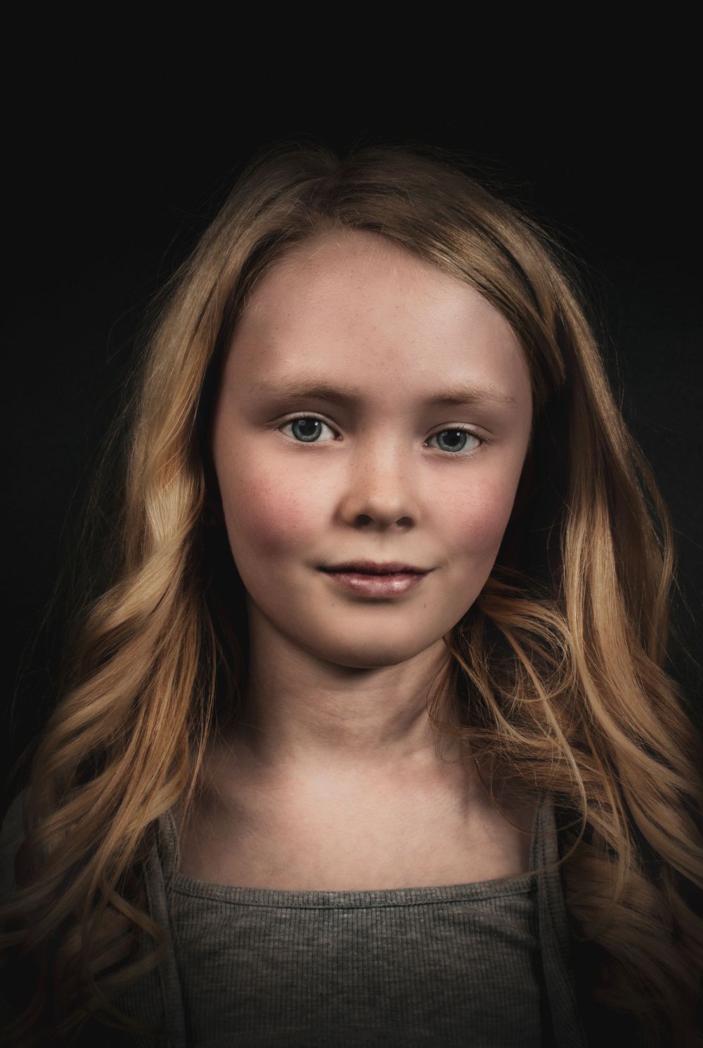 Moody dramatic studio portrait with soft lighting of a young person in a dark top against a black background.