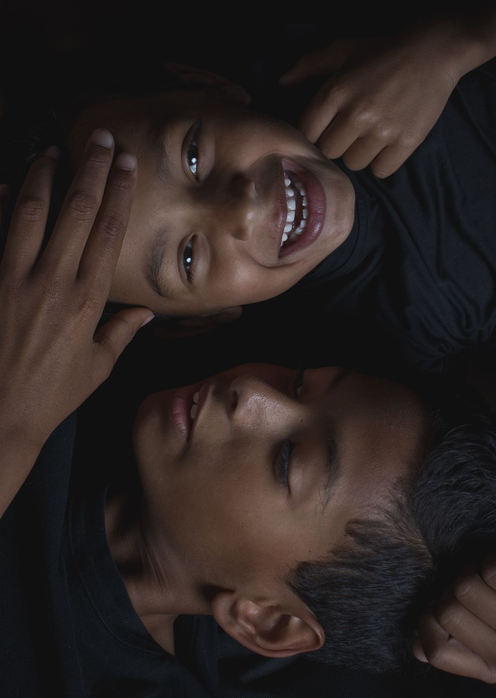 Two people lying down in dark lighting with contrasting expressions in dramatic shadows.