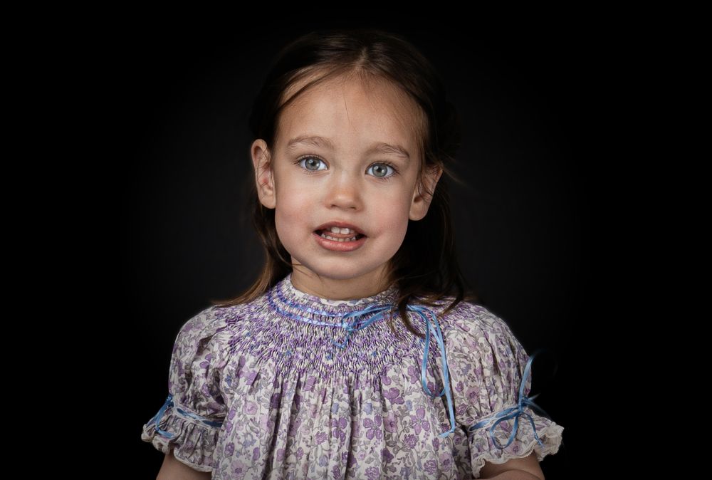 Child wearing a vintage floral smock dress with ruffled sleeves poses against dark background.