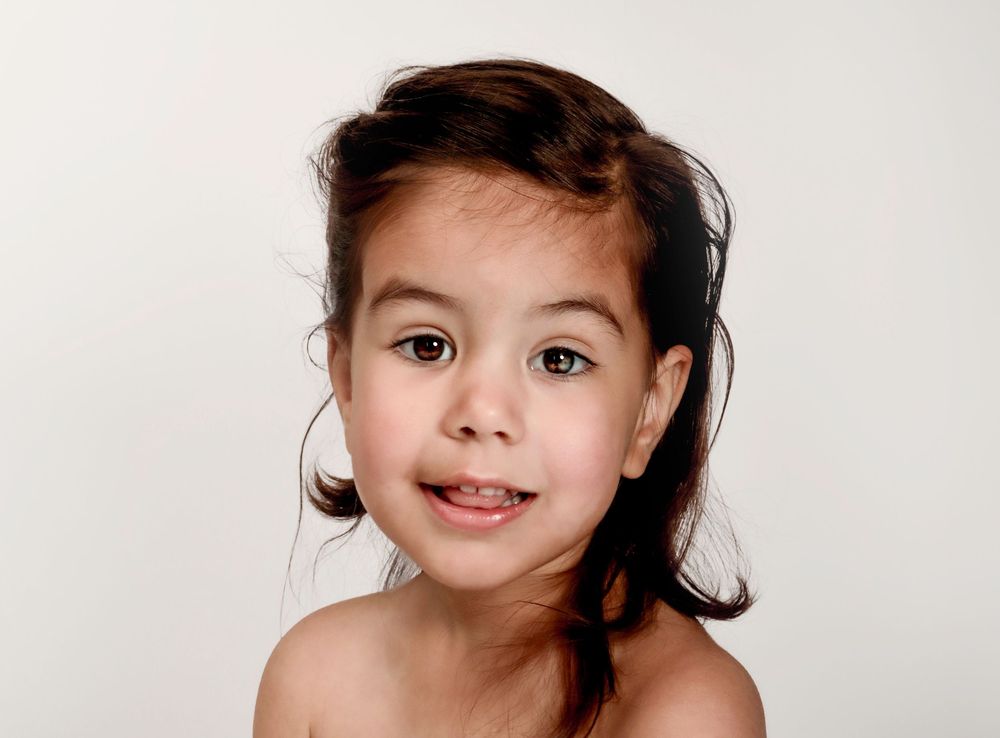 Smiling child with dark hair against white background in portrait style photography.
