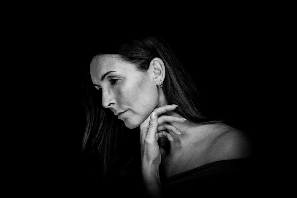 Dramatic black and white portrait in profile view showing elegant features and bare shoulders against dark background.