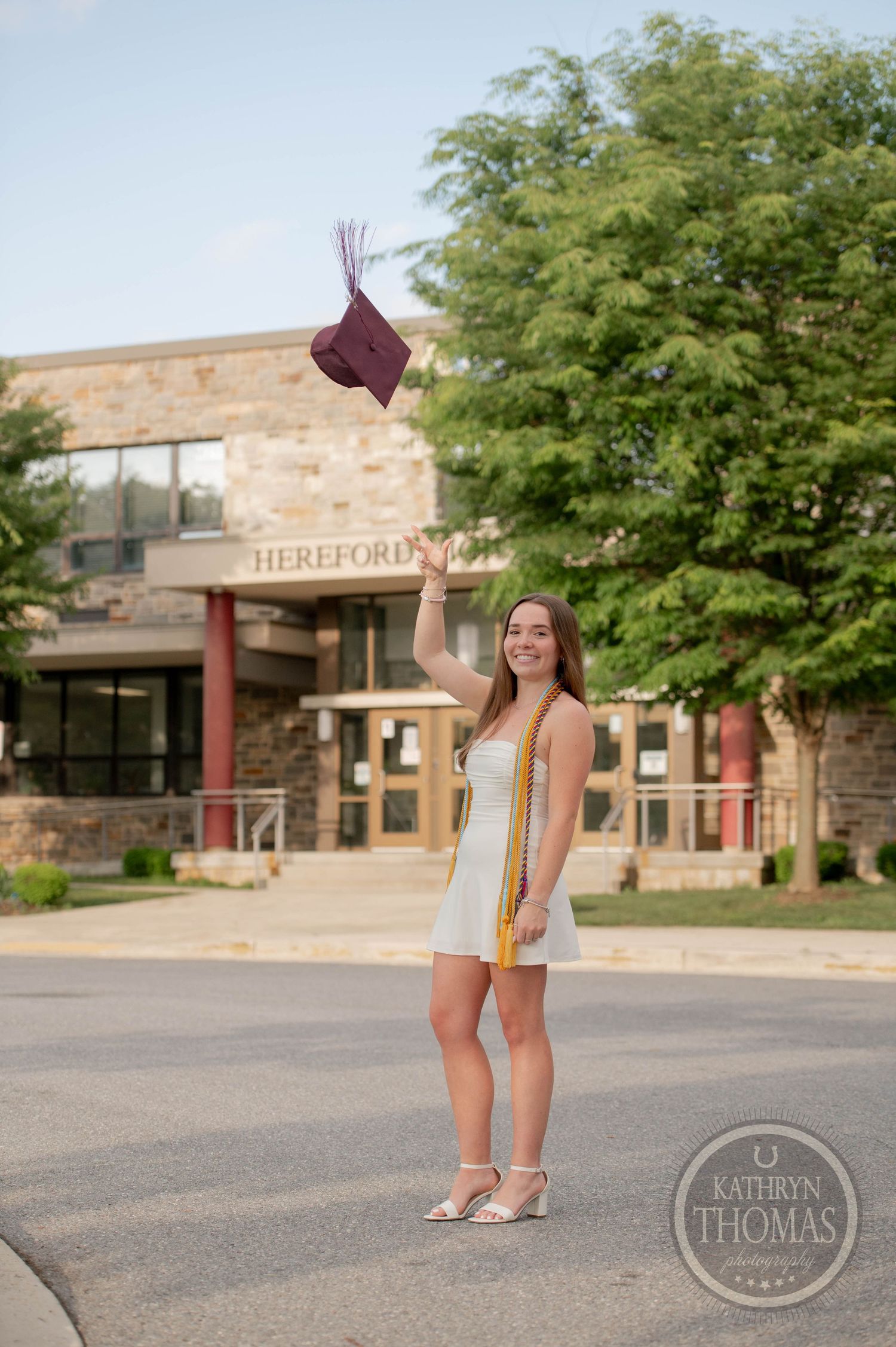 Graduate stands in front of Hereford High School entrance holding diploma during outdoor graduation photo shoot.
