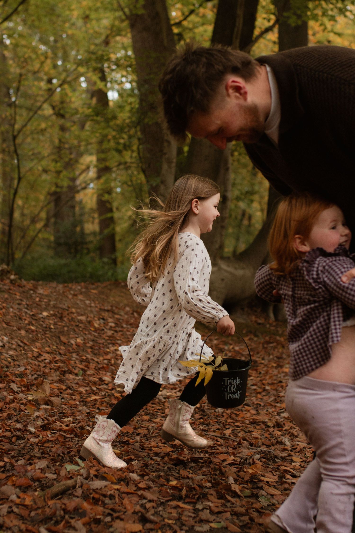 Children playing in a forest covered with fallen autumn leaves.