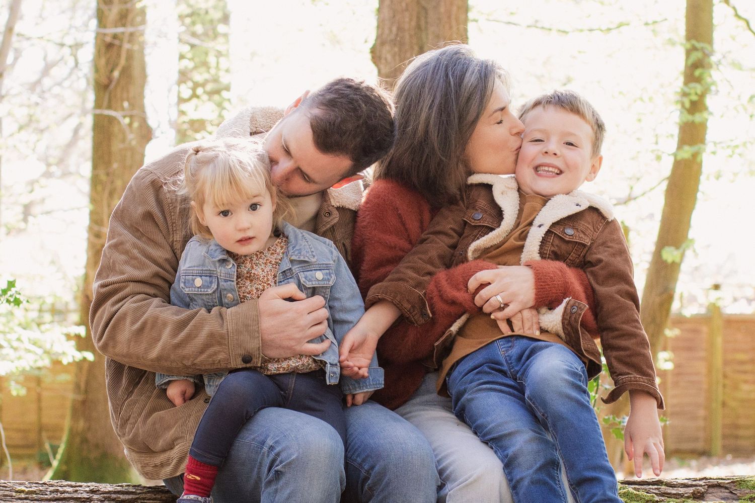 Family sitting together on fallen tree trunk in sunlit forest.