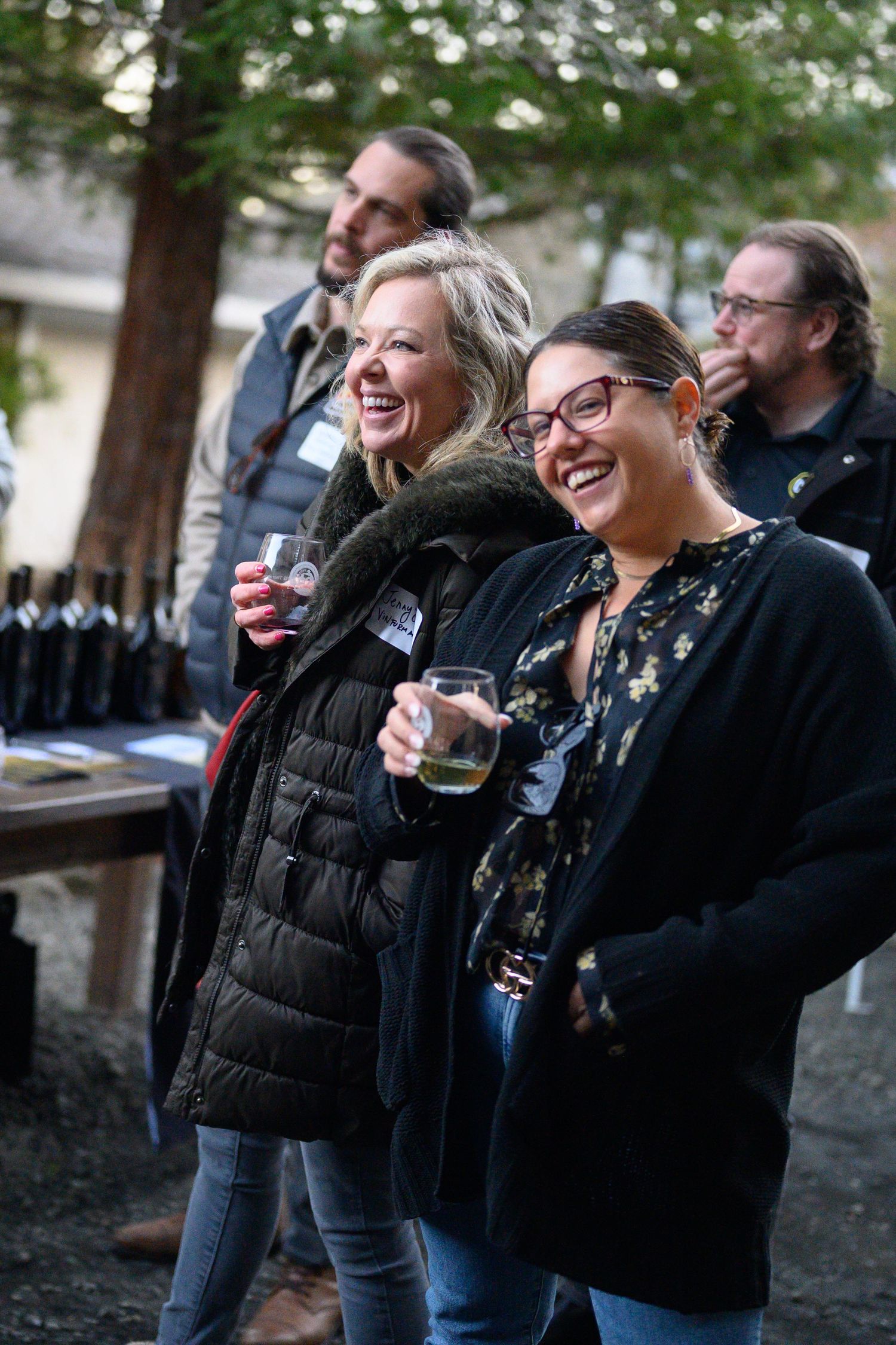 A group of friends share laughs while enjoying wine at an outdoor wine tasting and networking event hosted by Reid Family Vineyard.