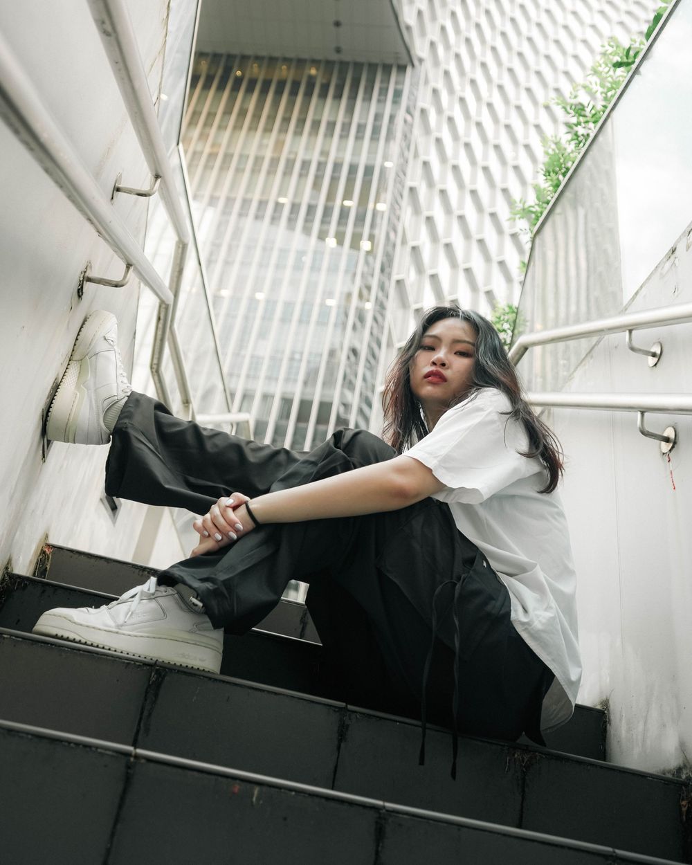 Person in white shirt and black pants sits on dark outdoor staircase with white walls.