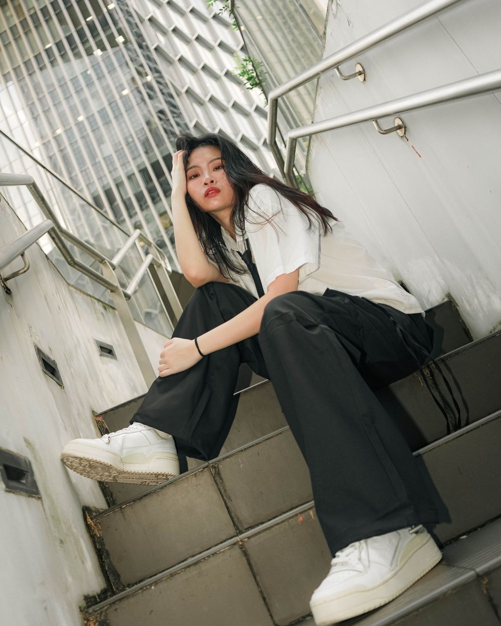 Someone in contrasting black and white outfit with white sneakers poses on concrete steps beside a wall.