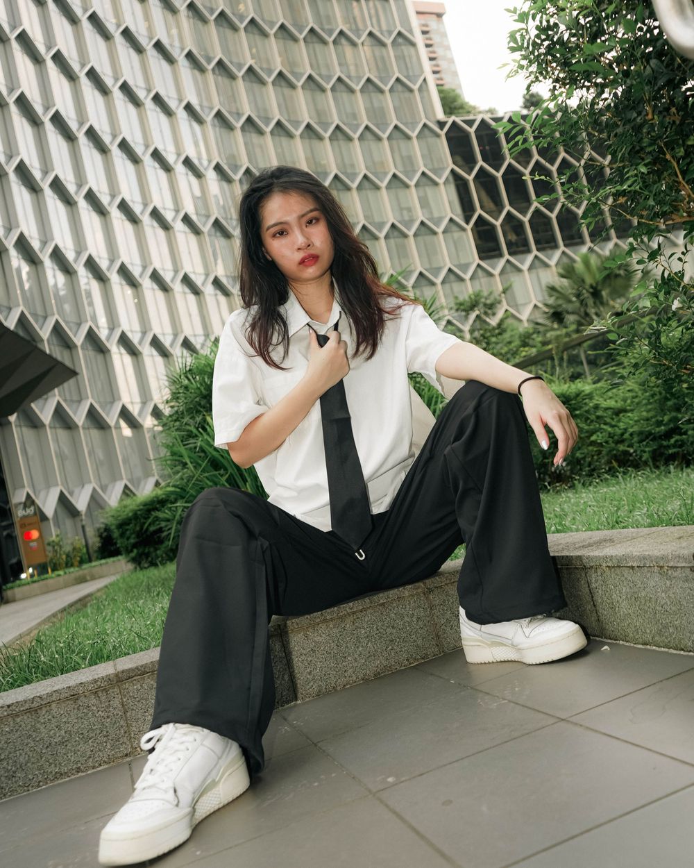 Casual monochrome outfit against geometric wall backdrop with white shirt, black pants and white sneakers.