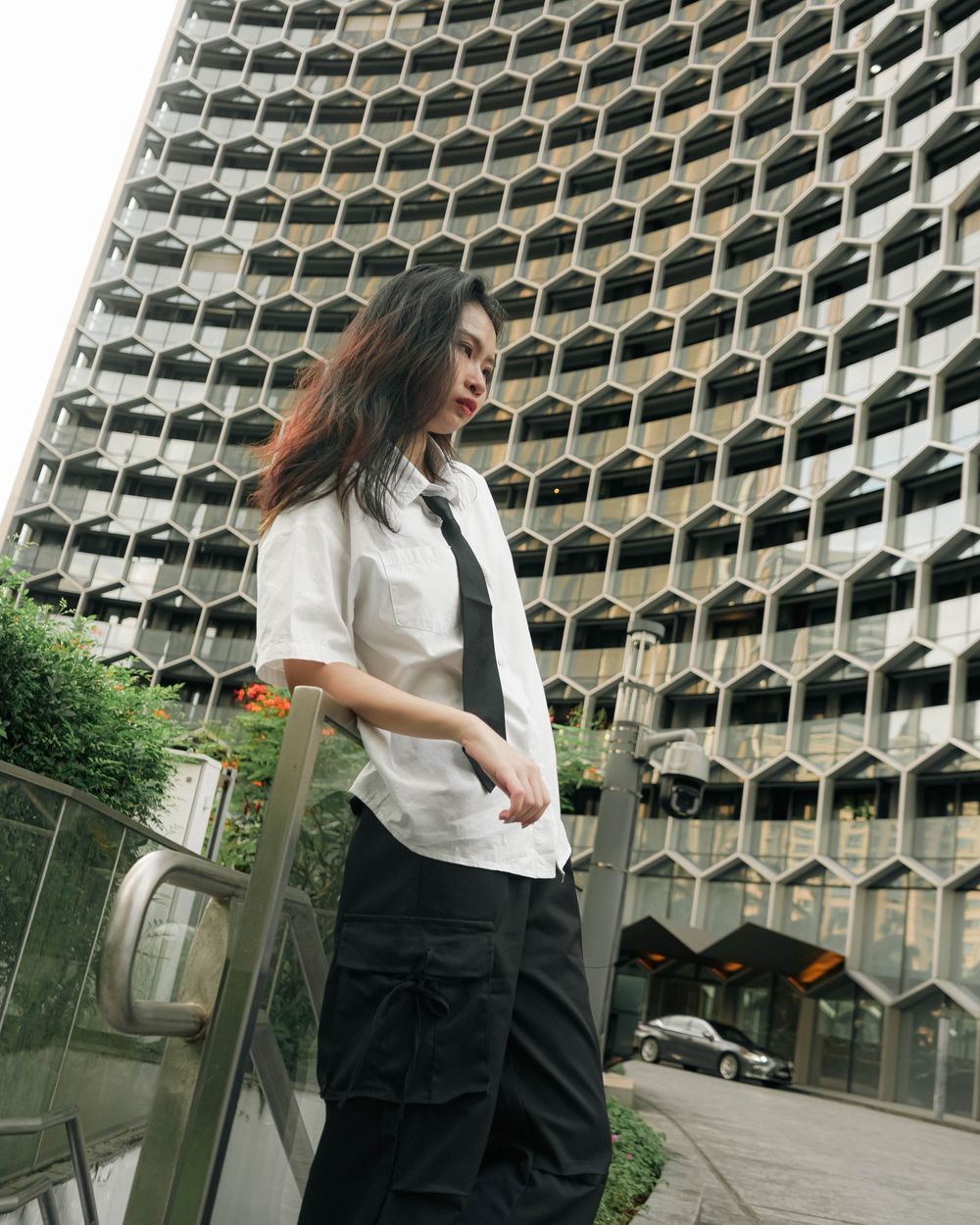 A stylish figure in white shirt and black pants stands against a striking geometric honeycomb-style building facade.
