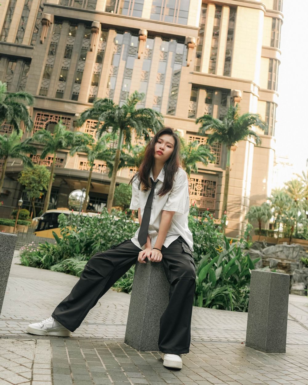 Four candid photos showing someone lounging and relaxing on stone benches near tropical plants in an urban setting.