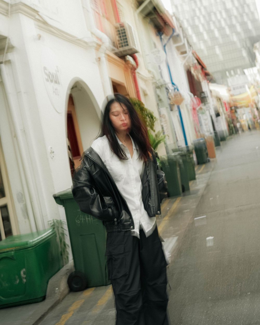 Figure in dark jacket walks past a white colonial-style building with ornate architectural details along an empty street.