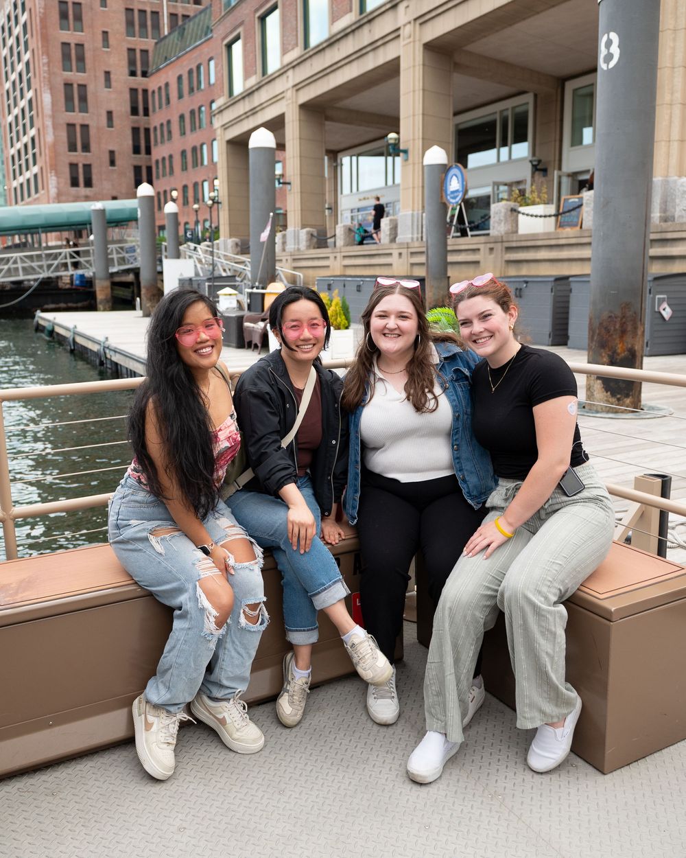A group sitting together on a waterfront deck outside a building with columns in an urban setting.