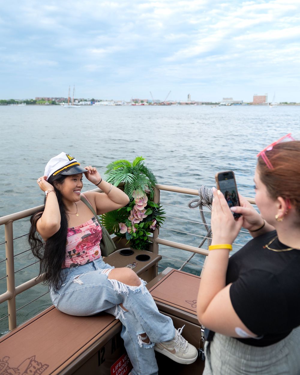 Group of people sit on a boat dock taking photos of the scenic waterfront view on a sunny afternoon.