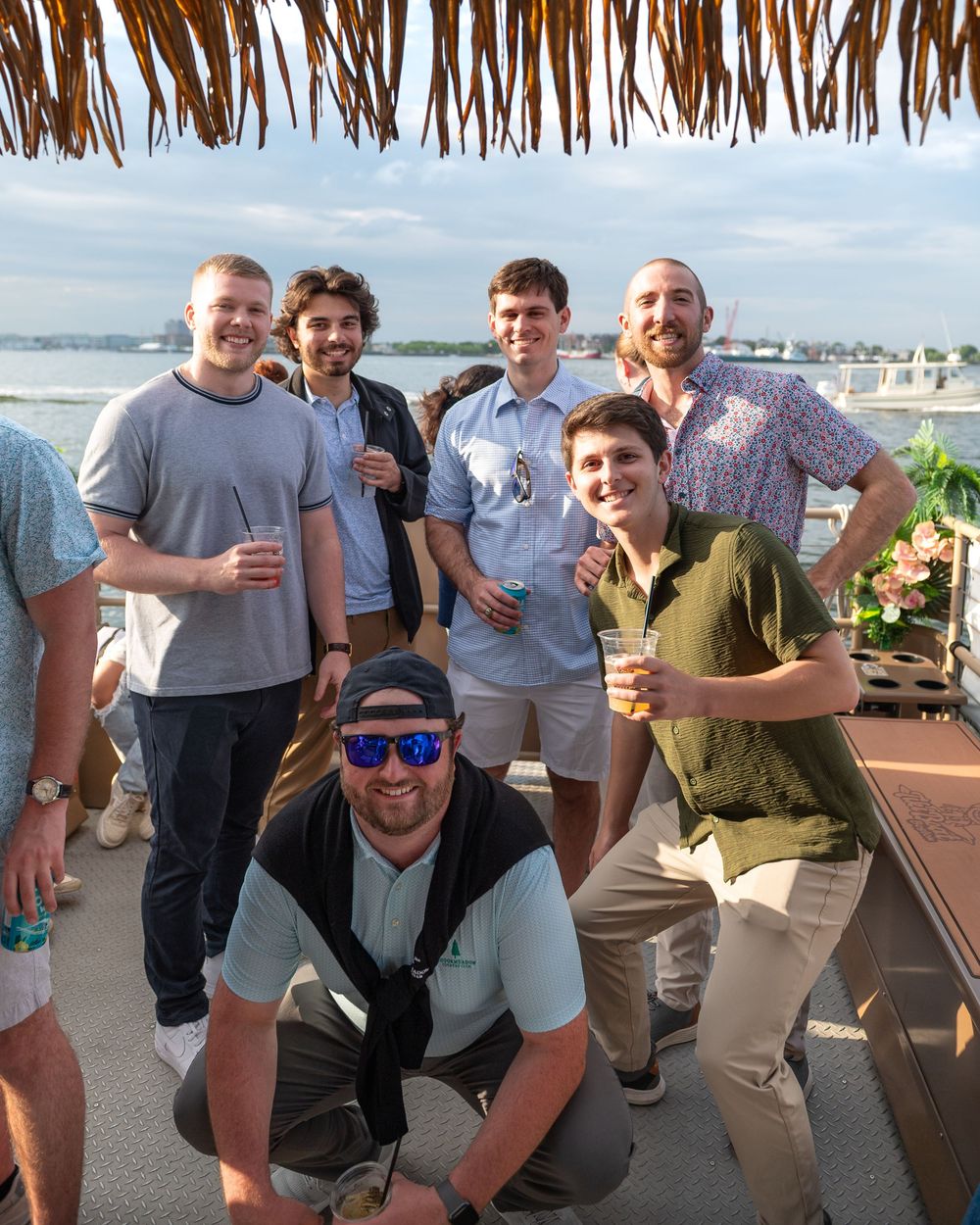 Group of friends posing together at a beachside venue with thatched roof and ocean views.
