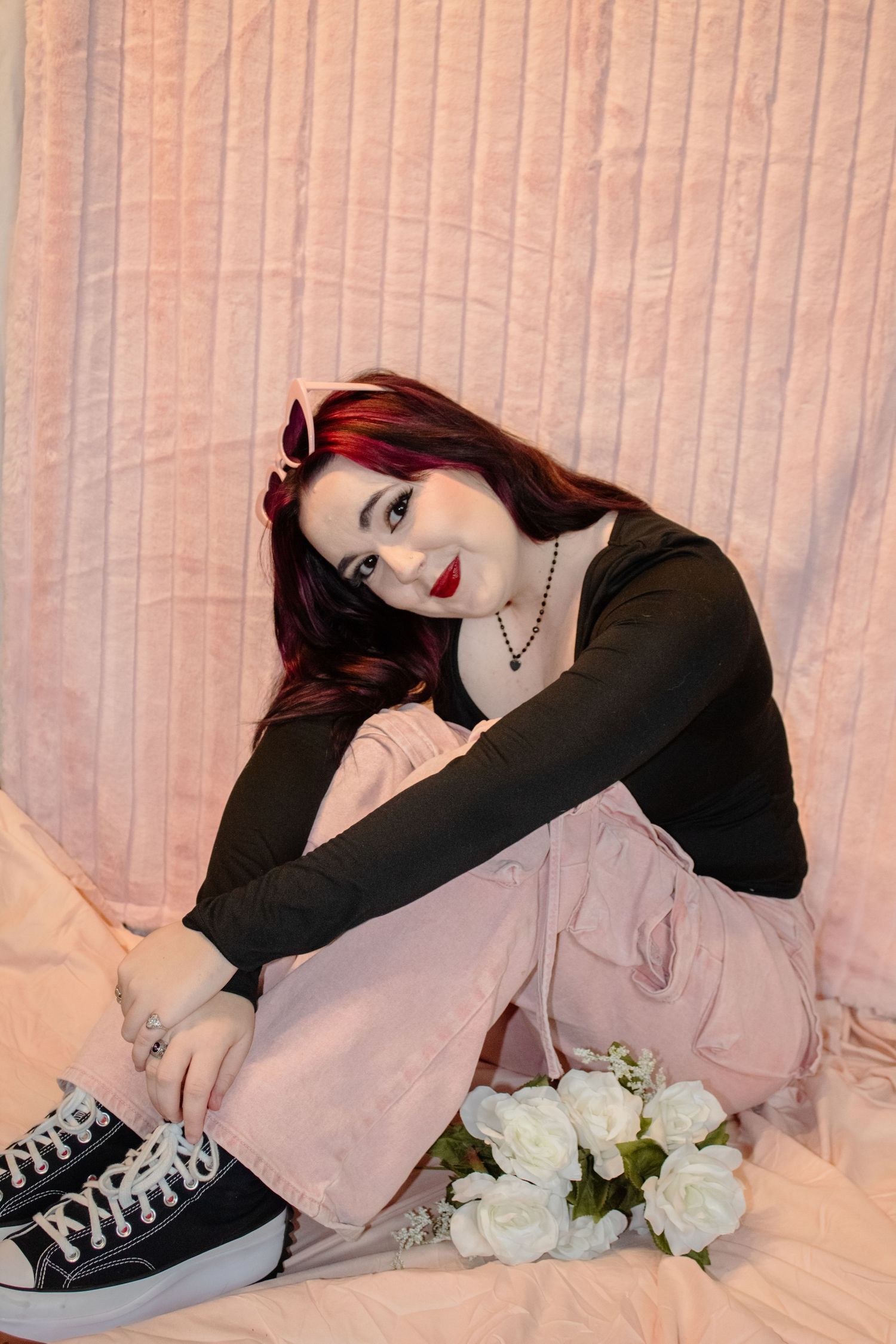 Four photos of someone wearing a black top with pink skirt lounging on a white couch with white roses visible.