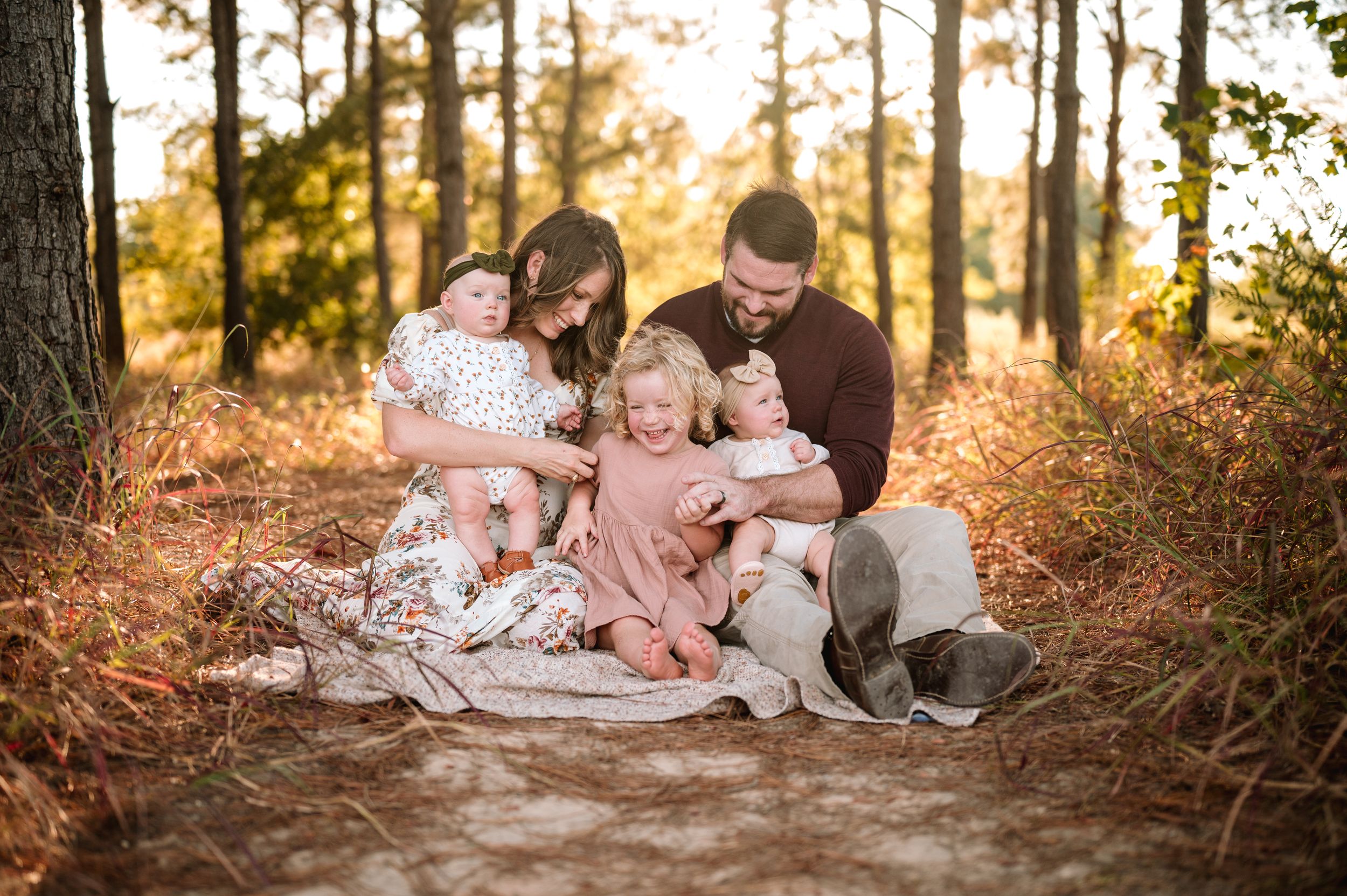A family sits together on a wooded path during golden hour sunset for a portrait session.