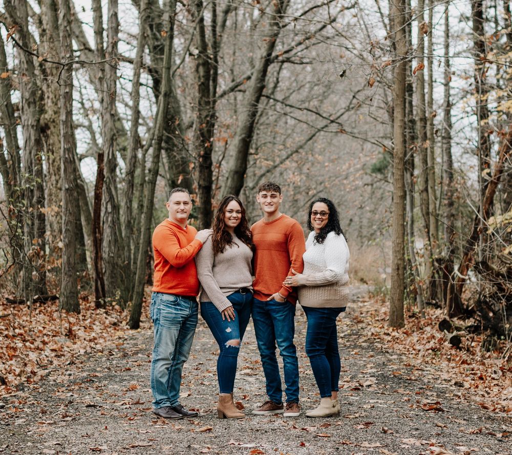 Four people in casual wear pose together on a tree-lined autumn path.