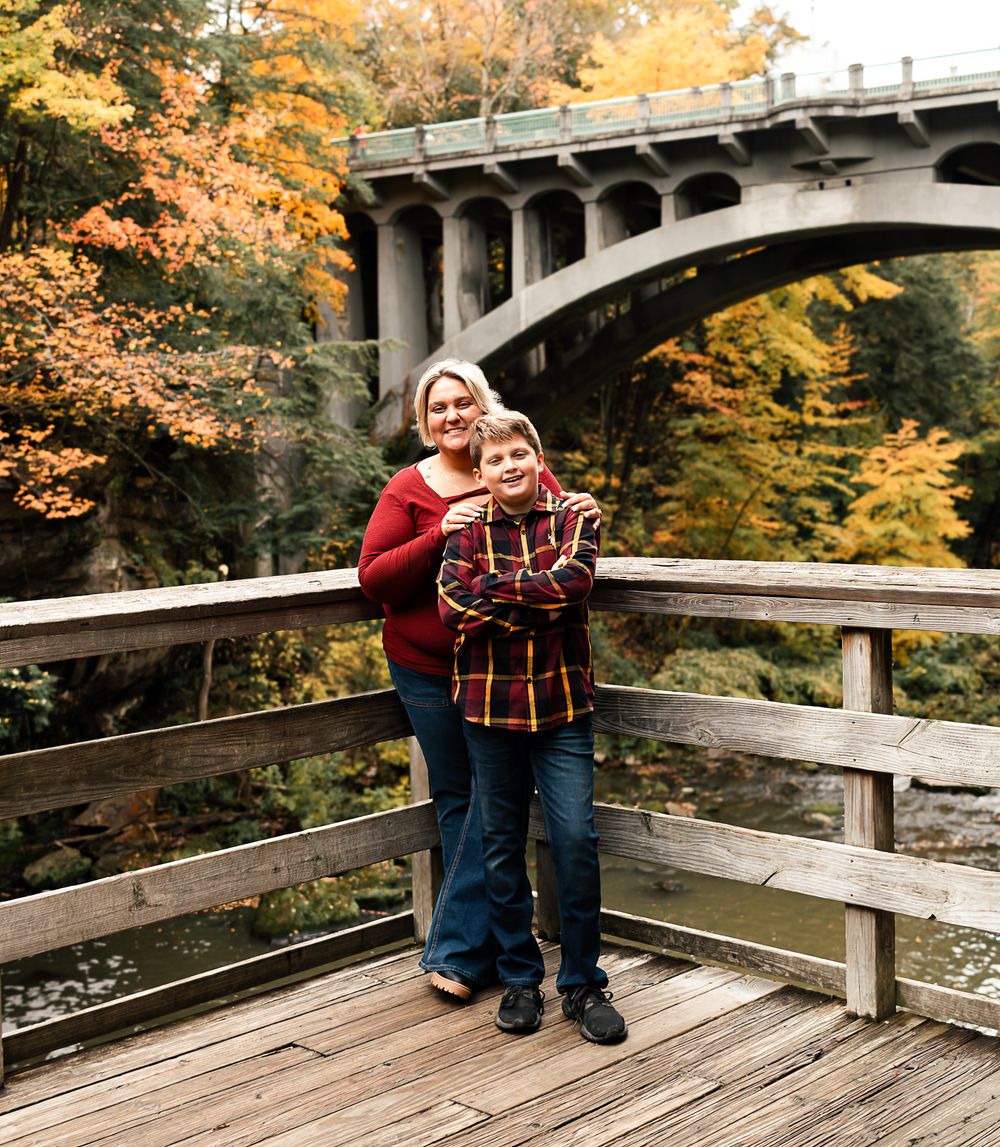 Scenic autumn photoshoot on a wooden bridge deck with fall foliage and stone architecture in the background.