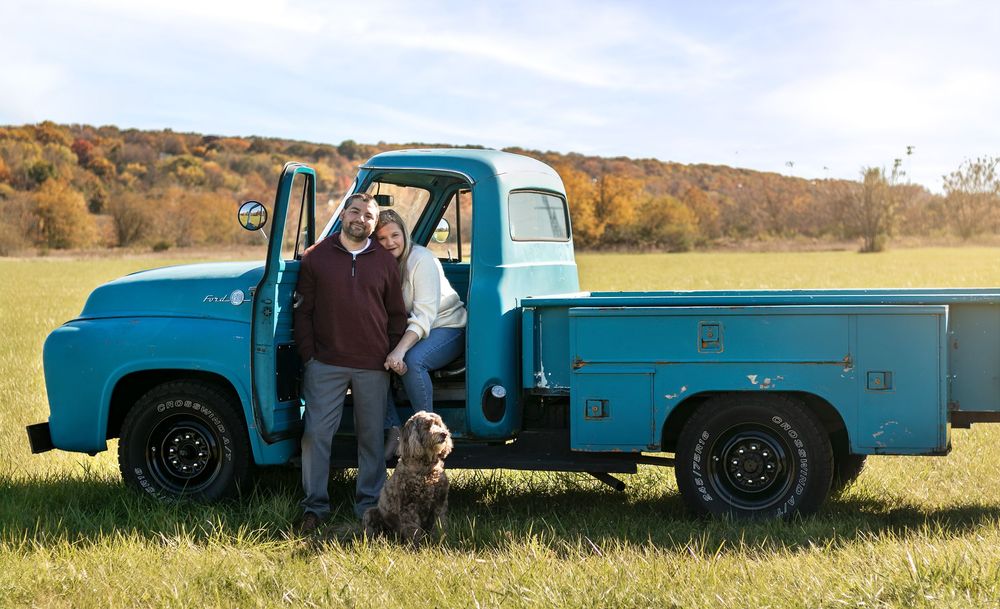 Classic blue Ford pickup truck parked in autumn field with two people and a dog standing beside it.fall family photos northeast ohio, collee