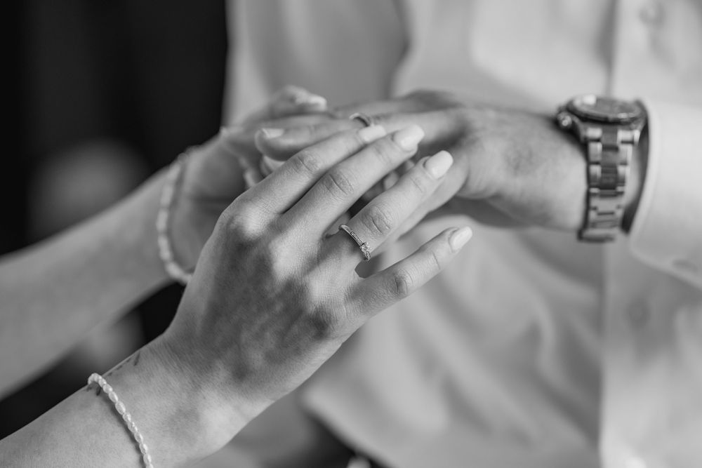 A black and white close-up shot of holding hands showcasing an engagement ring and watch.