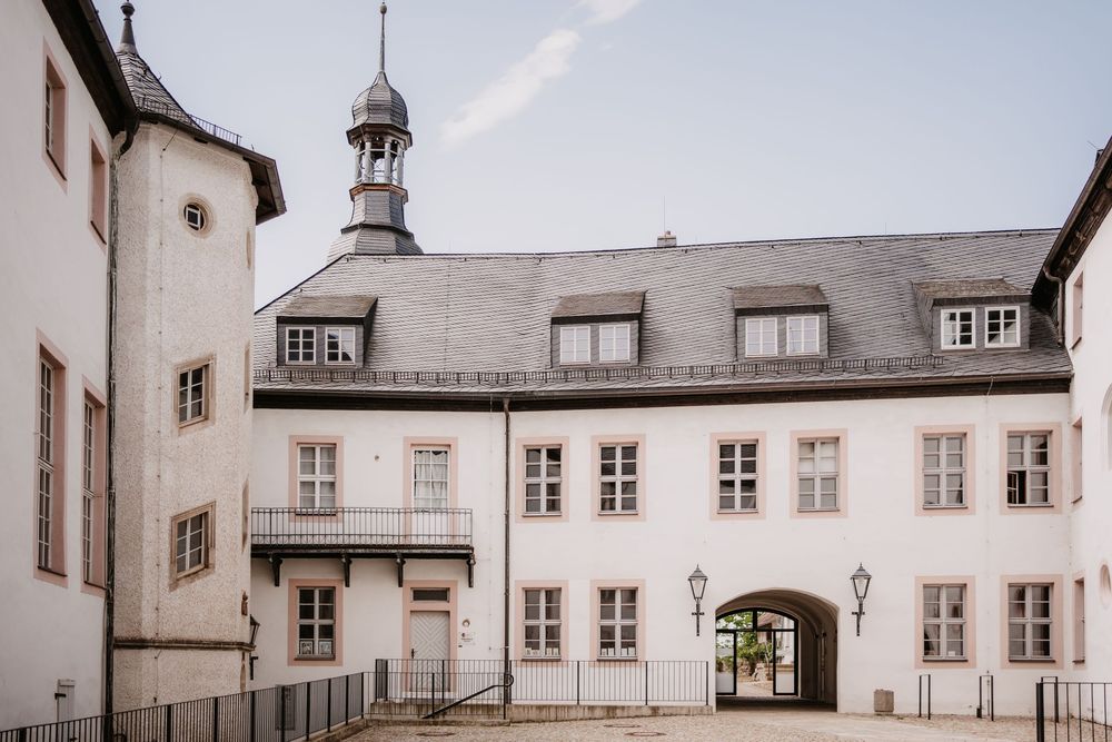 Historic white European building with dormer windows, tower spire and arched passageway in traditional architectural style.