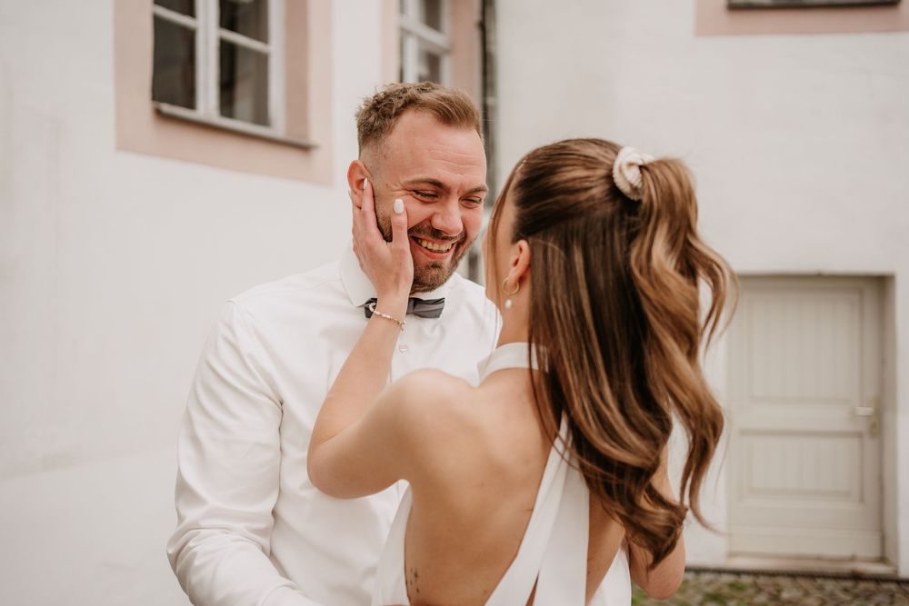 A happy couple shares joyful moments together during a photo session in formal white attire outside a building.