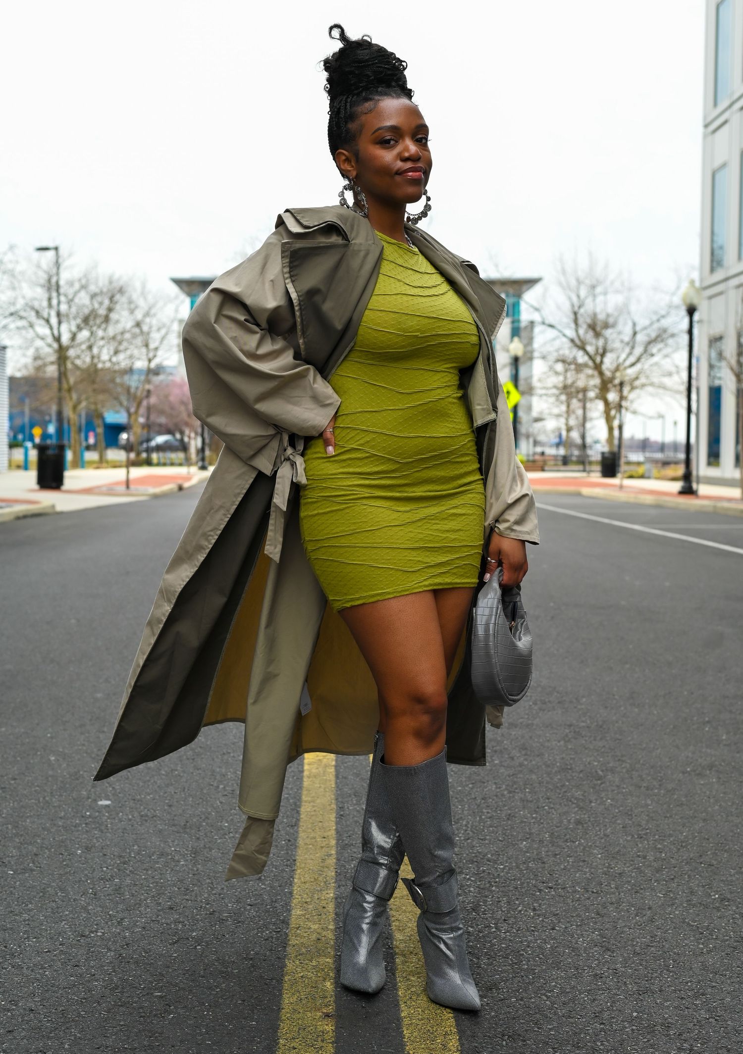 A stylish street fashion look featuring a beige trench coat paired with a neon green dress and silver boots.