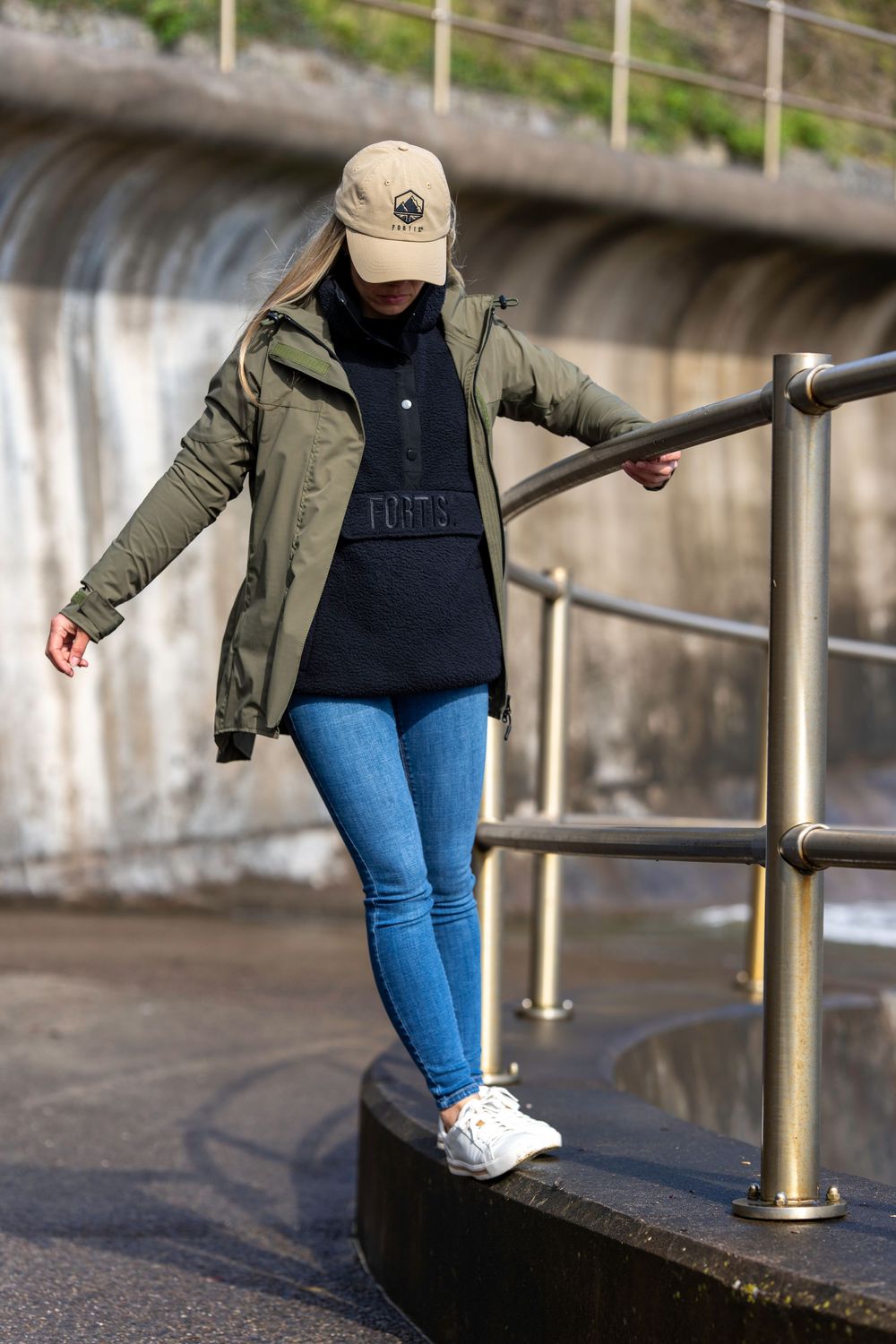 Someone wearing jeans and olive jacket walks up stone steps while holding a metal railing on a cloudy day.
