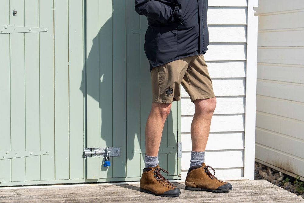 A pair of work boots on the front porch standing next to white siding with green shutters.