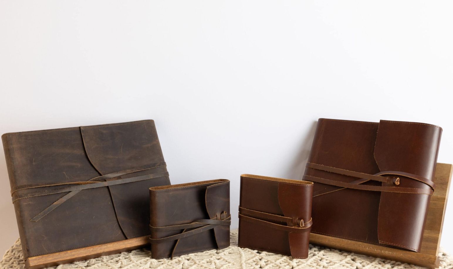 Four handmade brown leather wallets of varying sizes arranged on a light-colored textured surface against a white background.