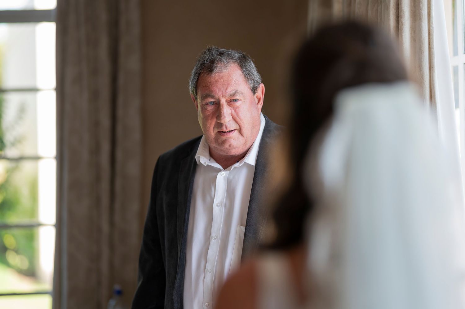 Wedding day moment captured through window light in formal attire.