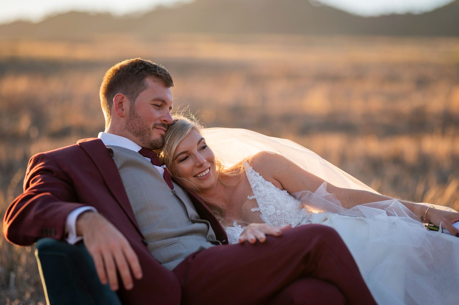 A couple relaxes in formalwear against a backdrop of golden sunset fields.